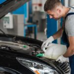 Mechanic pouring lubricant oil into car engine for maintenance.