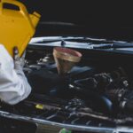 Professional oil specialists pouring fresh oil into car engine during maintenance