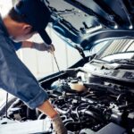 Mechanic checking engine oil level with dipstick during vehicle maintenance to prevent breakdowns